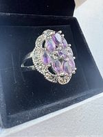 Close-up side view of the silver ring with purple gemstones in black velvet interior of the box.