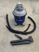 Front view of Shop-Vac vacuum with attached hose and cleaning accessories spread around unit on concrete surface.