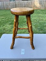Side view of solid wood stool showing round seat and three legs with natural branch details and two crossbars.