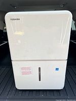 Front view of white Toshiba dehumidifier with logo, water level window, and sticker.