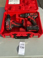 Two Milwaukee 2606-20 cordless drills placed inside a molded red plastic carrying case on a white surface. One drill has an attached M18 REDLITHIUM battery. Instruction manual is visible inside the case lid. The case is open and lying flat.