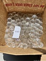 Box filled with many small clear faceted crystal prisms, showing quantity and condition.