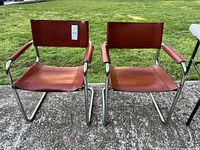 Front view of pair of vintage leather chairs showing brown leather seats and backs with chrome cantilever frames and padded armrests.