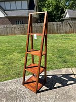 Full view of the tall wooden shelf on an outdoor concrete surface with grass and fencing in the background.