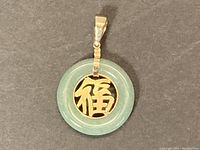 Overall view of green jade donut pendant with gold character on black background