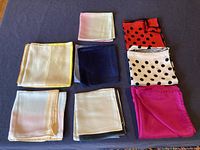 Top-down view of 8 folded silk scarves showing various colors and patterns including polka dots and solid colors.