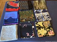 Photo of nine folded vintage silk scarves in various colors and patterns laid on a dark surface.
