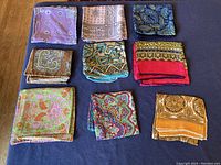 All nine scarves folded and arranged on a flat surface, showing the diversity of color and pattern.