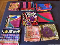 Overview photo showing all 9 vintage silk scarves laid out flat in three rows of three, various bright color patterns visible, scarves large to extra-large in size.