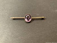 Front view of the antique bar brooch showing the gold bar and oval purple amethyst stone.
