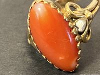 Close-up of oval red coral stone set in scalloped 22K gold bezel showing stone surface and setting details