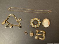 Full assortment of gold filled jewelry including charm bracelet, brooches, buckle, lock charm, and earrings on black background.