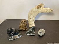Five Inuit stone carvings displayed on a dark surface: curved human figure, seal, owl, and two birds.