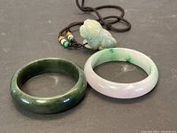 Two jade bangles side by side with carved jade pendant and cord visible