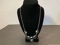 Full view of Navajo turquoise necklace displayed on black jewelry bust showing front pendant arrangement with five turquoise stones in circular silver settings.