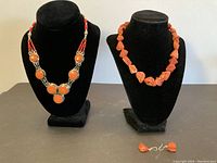 Pair of stone necklaces displayed on black velvet necklace stands with coral-colored drop earrings below.