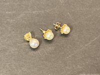 Pair of pearl stud earrings and pearl pendant displayed on dark fabric background showing front side.