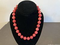 Full view of the ruby bead necklace on a black jewelry display stand showing the round faceted red beads and the silver spacers.
