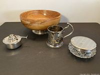 Four items displayed: wood bowl, silver tea glass holder, crystal jar and oil burner on black surface