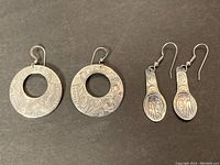Two pairs of silver earrings with Haida indigenous art designs against black background.