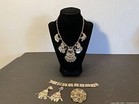 Full view showing necklace on display bust, bracelet, brooch, and earrings laid flat on surface.