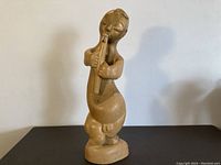 Front view of the wood carved boy playing a flute statue, showing full figure and flute held at mouth.