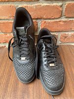 Top-down view of black Nike Air Force 1 sneakers showing woven detail on toe box, laces, and tongue with Nike branding.