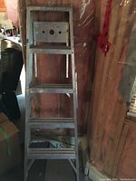 Front view of the 5-foot aluminum step ladder with five steps, standing against a wall.