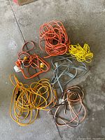 Photo showing various extension cords in orange, yellow, gray, and copper colors spread on concrete floor.