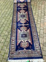 Full view of navy blue carpet runner with peach and taupe tones and geometric patterns, rolled at one end showing length and width.