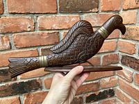 Side view of carved wooden pheasant figurine stand held in hand against brick wall background