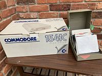 Original Commodore 1541C Disk Drive box with logo and model number, cardboard surface with brick wall background.