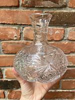 Crystal decanter held by hand in front of a brick background, showing the intricate cut glass designs and overall shape.