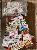 Multiple Indian bracelets in original packaging displayed in a plastic bag and loose on a brick surface. Various styles including floral and bead designs on red thread.