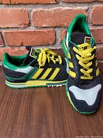 Side and front profile view of Adidas men's sneakers showing the black, green, yellow, and white color scheme and signature Adidas stripes.