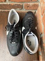 Top view of both black and white Nike sneakers placed side by side on wooden floor against brick wall.