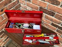 Red metal toolbox open showing assorted hand tools including screwdrivers and small containers