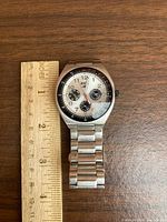 Front view of the men's Roots wristwatch on wooden surface with measuring ruler showing diameter of about 1.5 inches.