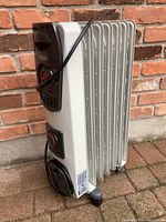 DeLonghi white floor space heater with several metal fins, rotary control knobs, and power cord coiled on the side.