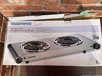 Photo of the Toastess stainless steel portable cooking range in original box showing two electric coil burners and control knobs