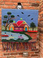 Full view of textile wall hanging depicting a colorful house, trees, birds, and grass with fringe detail at bottom.