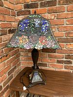 Full view of Tiffany style lamp showing stained glass shade with floral pattern and bronze/metal base with claw feet.