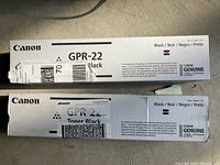 Two boxed Canon GPR-22 black toner cartridges stacked on a flat surface, showing front and side of packaging with brand and product details.