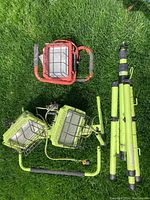 Overview of all four work lights, three green Power Light models, one red light, and disassembled green tripod stand parts on grass