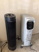 Black Holmes tower heater and white Comfort Zone oil-filled radiant heater side by side showing overall condition and design.
