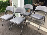 Four grey upholstered folding chairs arranged outdoors near a garage door.