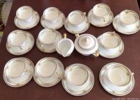 Photo of 12 teacups with matching saucers, sugar bowl and creamer arranged on a table