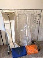 Full view of metal rolling clothing rack with hanging garment bags and two garment folding packs laid on floor.