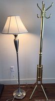 Polished nickel floor lamp illuminated next to brass hat rack showing overall style and size.