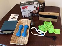 Overall view of fitness items including UFC stability ball box, dumbbells, resistance bands, hand weight with rope, food scale, and an unknown black boxed item.